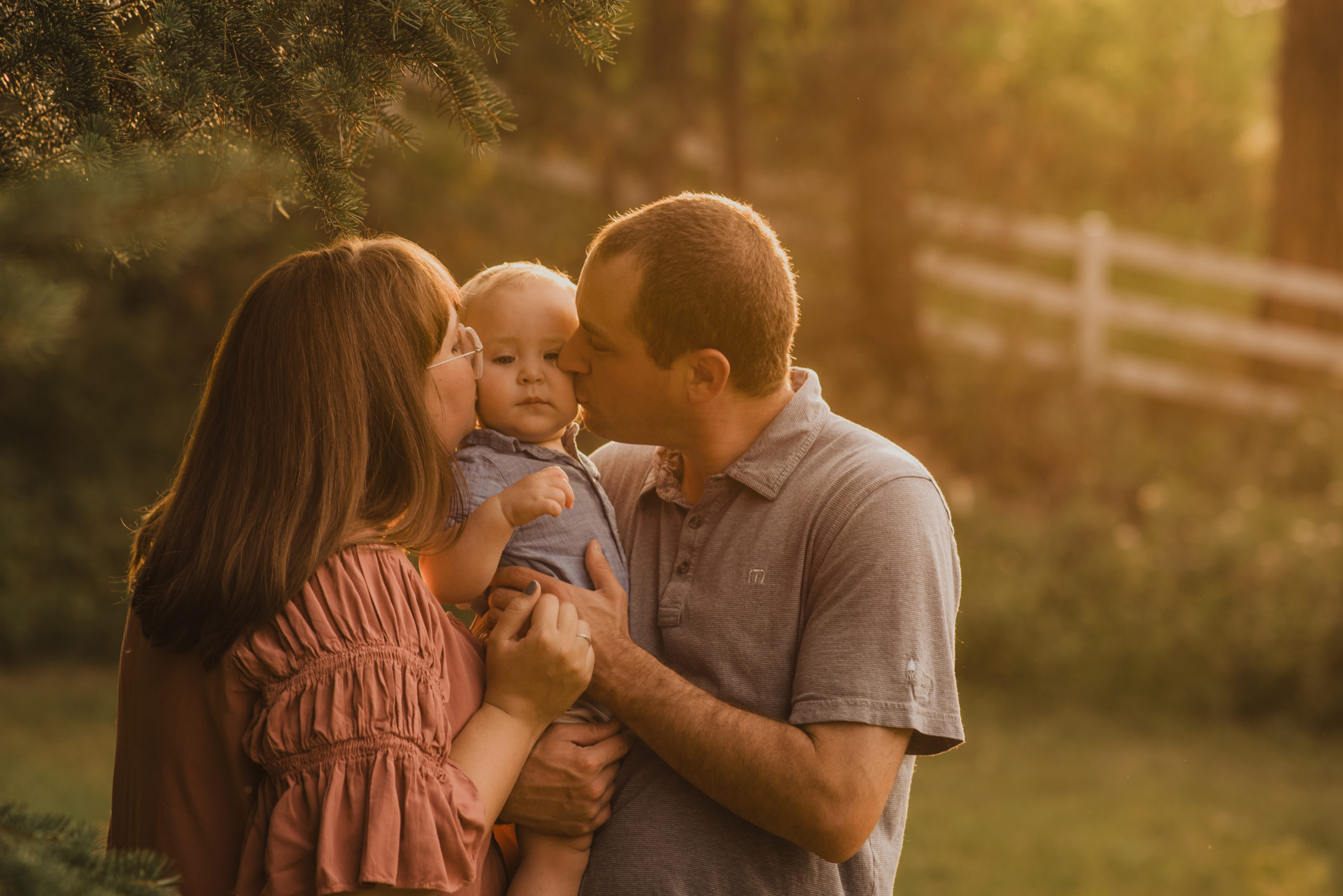 A mother and father kissing their baby boy in a ray of sun in Kalispell, Montana.